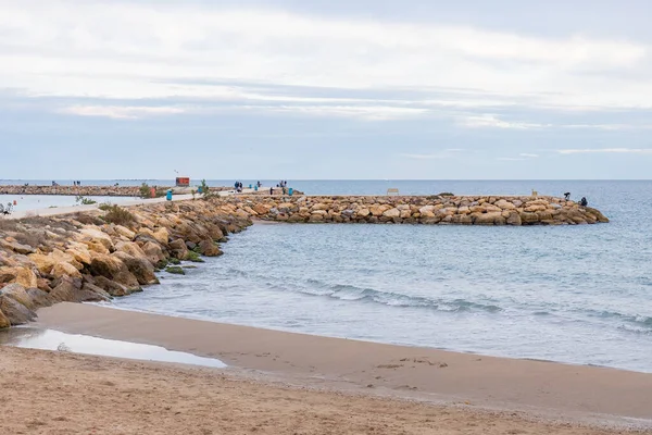 Kumlu bir sahil denize doğru kıvrılır ve uzun, kayalık bir dalgalanma suya doğru uzanır. Dalgakıran, balıkçılık ve yürüyüş, Guardamar, İspanya ve Akdeniz boyunca çok sayıda insan görülebilir.