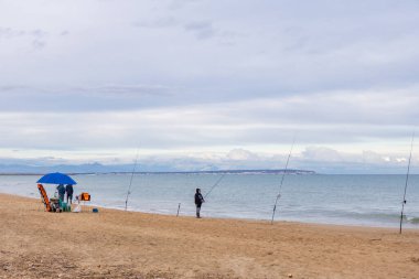 Alicante, İspanya - 17 Ocak 2026: Çürük bir kumsalın altında, Guardamar del Segura 'da deniz kenarında sakince balık tutan balıkçılar