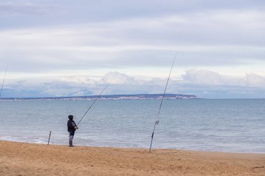 Alicante, İspanya - 17 Ocak 2026: Çürük bir kumsalın altında, Guardamar del Segura 'da deniz kenarında sakince balık tutan balıkçılar