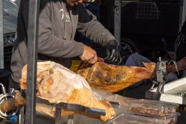 Guardamar del Segura, İspanya - 25 Ocak 2026: Bir satıcının geleneksel bir stantta korunan bir İspanyol jambonu dilimlediği yerel bir sokak pazarı