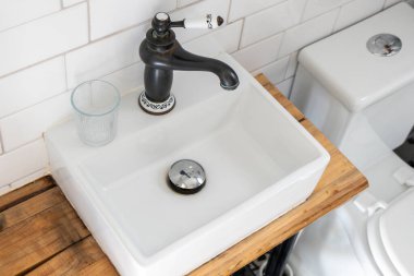 Modern banyo içi beyaz metro fayansları, kare seramik tezgah lavabosu, ve beyaz seramik detaylarla siyah vintage çeşmesi, çağdaş ve retro tasarımı harmanlayan