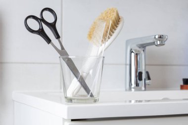 Modern minimalist beyaz banyodaki lavabonun yanındaki banyo musluğunun yanında saç makası ve tarak.