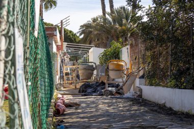 Beton mikser ve araçlara sahip bir inşaat sahası, bir yerleşim sokağında aktif çalışmaları gösteriyor, kentsel gelişim ve altyapı temasını vurguluyor