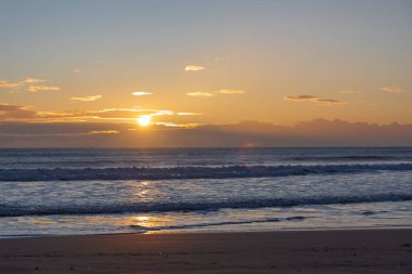 A golden sunset over the Mediterranean Sea in Spain, capturing a serene beach scene with waves gently lapping at the shore, perfect for a tranquil