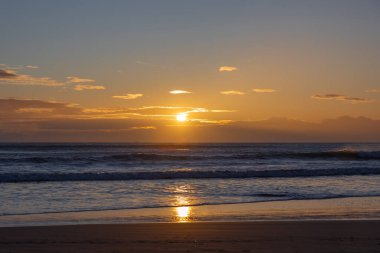 A serene sunset over the Mediterranean Sea in Spain, with gentle waves lapping at the shore, capturing the tranquil beauty of the coastal landscape.