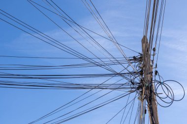 Parlak mavi gökyüzü boyunca uzanan sayısız güç ve iletişim hatlarına sahip bir elektrik direğinin alçak açılı görüntüsü. Elektrik ve ağ bağlantılarını vurgulayan kentsel altyapı kavramı