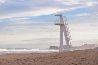 İspanya, Torrevieja 'nın kumlu sahilinde kıyıya vuran dalgalarla okyanusa bakan beyaz bir cankurtaran kulesi var..