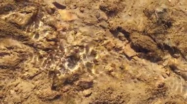 Detaylı bir yüksek açı görüntüsü, İspanya 'da kayalık ve kumlu bir nehir yatağının üzerinden akan sığ, temiz bir su görüntüsü yakalar. Altın güneş ışığı zeminde parlak, yakıcı desenler oluşturur.