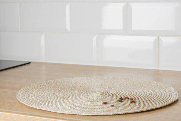 Empty space background. A rustic, round woven placemat rests on a wooden kitchen counter, with a few coffee beans scattered on its surface, suggesting a cozy morning coffee break.