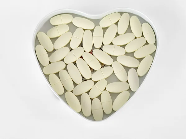 Pillole gialle In una scatola a forma di cuore, isolata sullo sfondo bianco . — Foto Stock