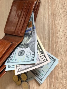 İçinde Amerikan dolarları ve Euro paraları bulunan kahverengi deri cüzdan, kısmen açık ve ahşap bir masanın üzerinde dinleniyor..