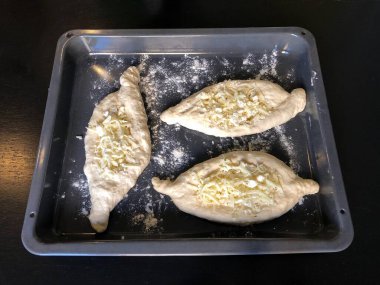 Çiğ Adjarian Khachapuri hamuru koyu, dikdörtgen bir pişirme çarşafında. Hamur, geleneksel tekne şeklinde şekillenir ve pişirmeden önce sulguni peyniri ile kaplanır. Gürcistan peynirli ekmeğin zanaatkar hazırlık süreci..