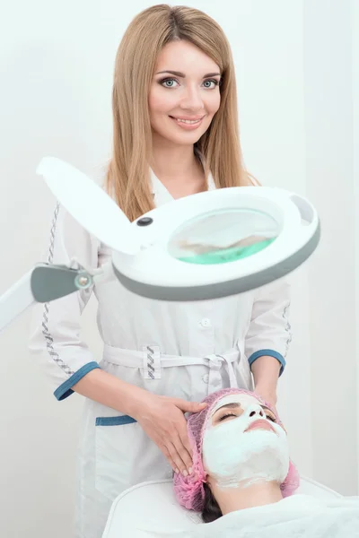 A beautiful lady cosmetician is making a face mask to her client in the beauty salon. — Stock Photo, Image