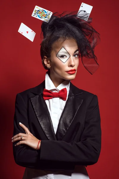 Retrato de una joven hermosa señora croupier con un maquillaje artístico comodín y tarjetas voladoras alrededor en el fondo rojo. Juego y concepto de casino. Captura de estudio . — Foto de Stock