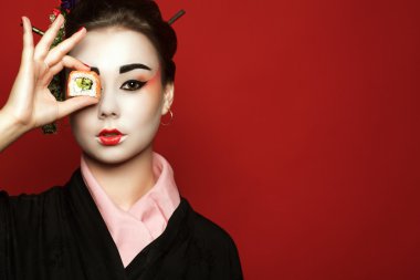 Suşi gözü önünde bir parça kırmızı zemin üzerine tutarak kimono içinde genç heisha portresi. 