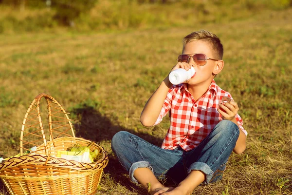 Menino elegante em óculos de sol está bebendo iogurte no prado — Fotografia de Stock