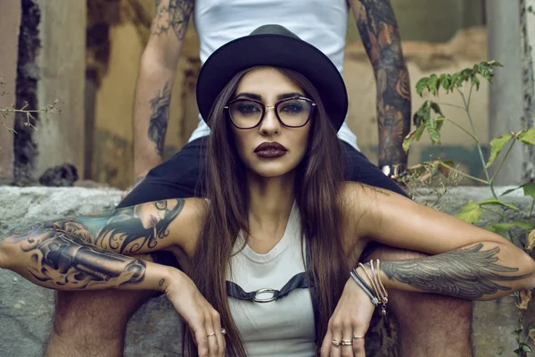 Splendida ragazza tatuata con trucco provocatorio seduta tra le gambe del suo ragazzo in un edificio abbandonato in rovina — Foto Stock