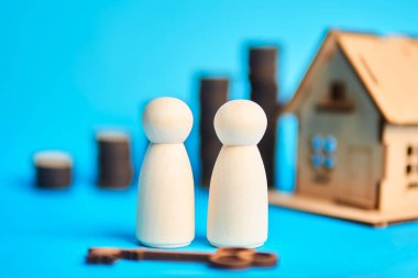 Bir ev ve anahtar yakınındaki iki ahşap figür ev alıcılarını ve ipotek onayını simgeliyor, mülk sahipliği kararlarını ve aile mali planlamasını temsil ediyor.