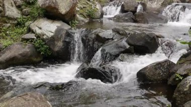 4K kusursuz kristal berraklığında dağ akıntısı karanlık kayaların üzerinden akıyor. Doğal ışıklandırma ve minimum renk derecelendirmesi. Rahatlama, doğa ve arka plan görselleri için ideal