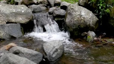 4K yatay berrak su döngüsü doğal ışık altında küçük bir dağ deresinde büyük kayalar arasında yavaşça akıyor. Huzurlu doğa geçmişi