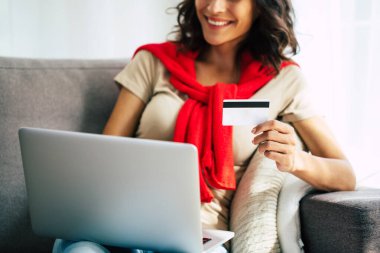 Günlük giysiler içinde güzel mutlu genç bir kadın evdeki kanepede oturuyor ve Kara Cuma 'da online alışveriş yapıyor..
