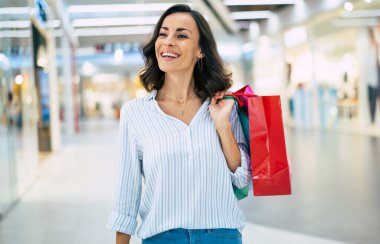 Renkli alışveriş torbalarıyla modaya uygun giyinmiş şık, genç ve modern bir kadın alışveriş merkezinde geziniyor.