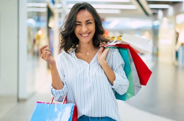 Renkli alışveriş torbalarıyla modaya uygun giyinmiş şık, genç ve modern bir kadın alışveriş merkezinde geziniyor.