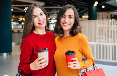 Alışveriş torbalarıyla iki zarif ve şık genç bayan alışveriş merkezinde yürürken Kara Cuma indirimi