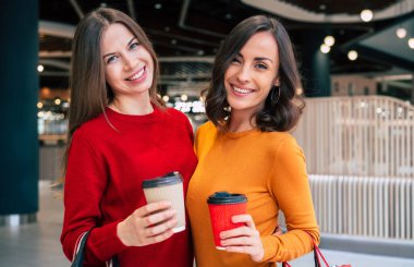 Alışveriş torbalarıyla iki zarif ve şık genç bayan alışveriş merkezinde yürürken Kara Cuma indirimi