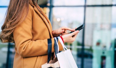 Çok sayıda renkli alışveriş çantaları olan, şık telefon ve kredi kartıyla şık bir genç bayan siyah cuma günü alışveriş merkezinde yürürken...