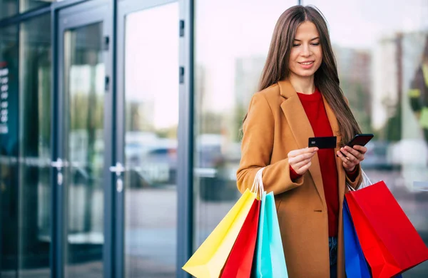 时尚而又漂亮的年轻女性 在购物后外出散步时 用智能手机做网上银行和购物袋 — 图库照片