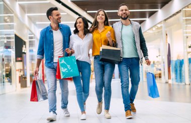 Alışveriş çantalı iki mutlu çift alışveriş merkezinde birlikte yürüyüp eğleniyorlar.