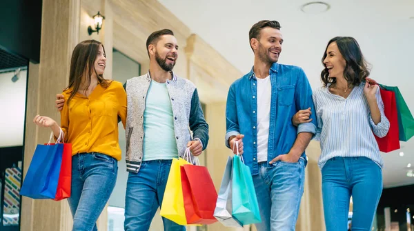 ショッピングの間にショッピングモールの中を歩いている紙の袋でカジュアルな服で興奮した美しい現代的なスタイリッシュな友人の幸せなグループ — ストック写真