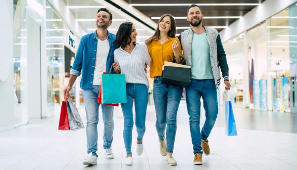 Happy group of excited beautiful modern stylish friends in casual wear with paper bags are walking in the mall during shopping.