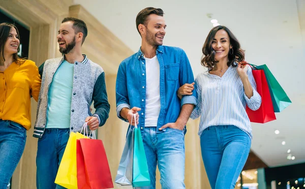 ショッピングの間にショッピングモールの中を歩いている紙の袋でカジュアルな服で興奮した美しい現代的なスタイリッシュな友人の幸せなグループ — ストック写真