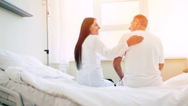 Mutlu doktor ve hastanın, arka plandaki klinik koğuşundaki yatakta otururken çekilmiş arka plan fotoğrafı.