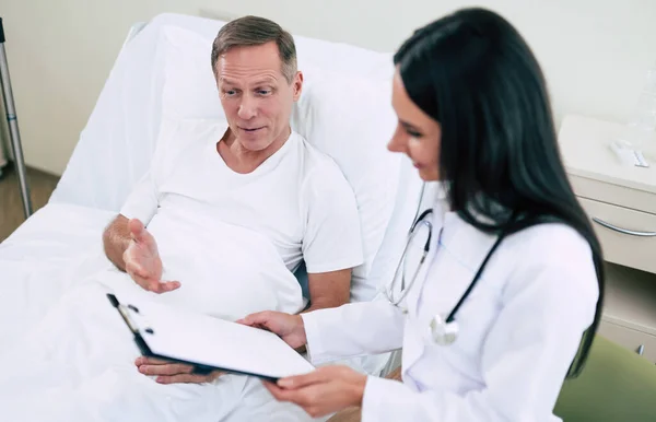 Yakışıklı Olgun Hasta Bir Adam Klinik Yatağında Uzanıyor Beyaz Önlüklü — Stok fotoğraf