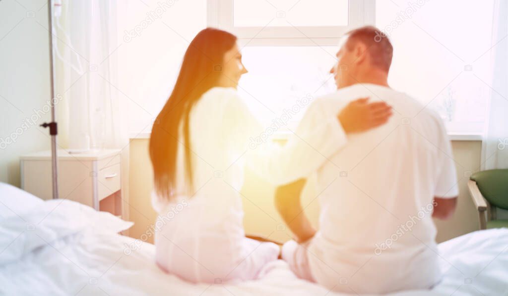 Back view photo of happy doctor and patient while they sitting on the bed in the clinic ward on the window background