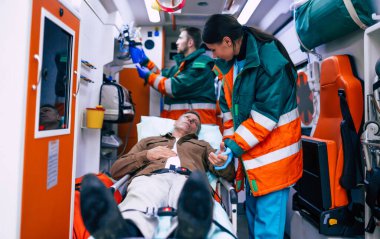 Sağlık görevlileri ambulansta sedyede yatan kıdemli bir hastayla ilgileniyorlar..