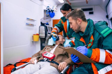 Doktorların acil durumu ya da sağlık görevlileri, yaşlı bir hastayla ambulansta sedyede yatarken birlikte çalışıyorlar..