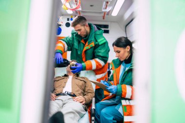 Ambulans arabasında iki profesyonel sağlık görevlisi ve sedyede bir hasta. 