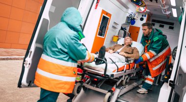 Kendine güvenen ve profesyonel doktorlar hasta bir hastayı hastane binasının yakınındaki bir sedyede ambulanstan boşaltıyor.