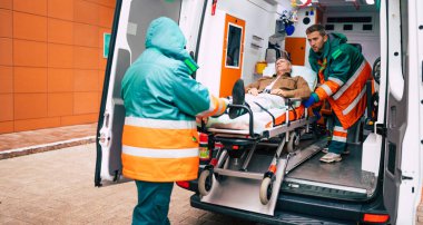 Kendine güvenen ve profesyonel doktorlar hasta bir hastayı hastane binasının yakınındaki bir sedyede ambulanstan boşaltıyor.