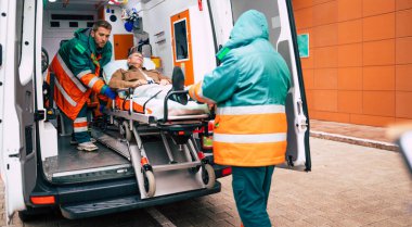 Kendine güvenen ve profesyonel doktorlar hasta bir hastayı hastane binasının yakınındaki bir sedyede ambulanstan boşaltıyor.