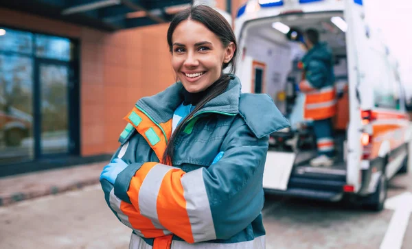 Professional and confident young woman doctor looking on the camera with ambulance background