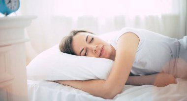 Harika genç esmer kadın evde dinlenirken büyük beyaz yatakta uzanıyor.