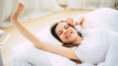 Harika genç esmer kadın evde dinlenirken büyük beyaz yatakta uzanıyor.