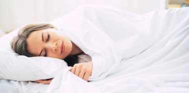 Harika genç esmer kadın evde dinlenirken büyük beyaz yatakta uzanıyor.