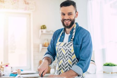 Yakışıklı, genç, sakallı adam ailesi için taze vejetaryen salatası pişiriyor ve büyük açık mutfakta eğleniyor.