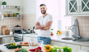 Sakallı, gülümseyen yakışıklı adam evde poz veriyor ve kameraya bakıyor.